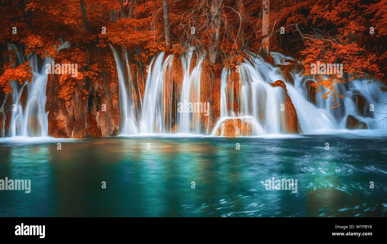 A long exposure of a beautiful set of waterfalls and water pool in a forest setting, with tree foliage and vegetation in fantasy autumn colors of vibr Stock Photo