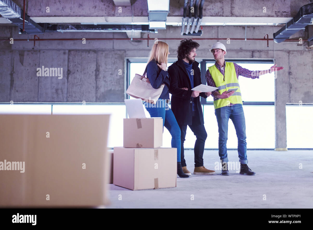 architect using tablet computer while showing house design plans to a young couple at construction site Stock Photo