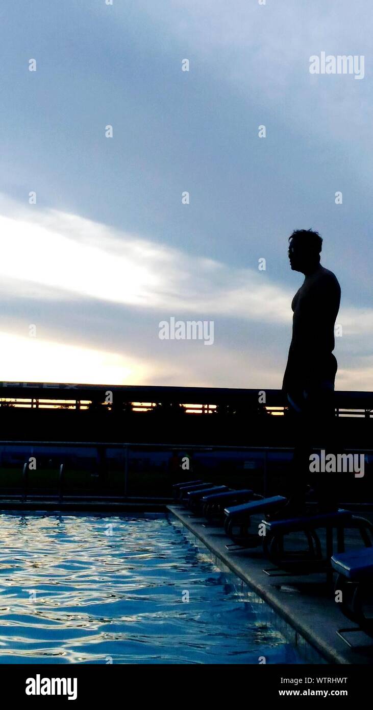 Silhouette Man Standing On Diving Board Against Sky During Sunset Stock Photo