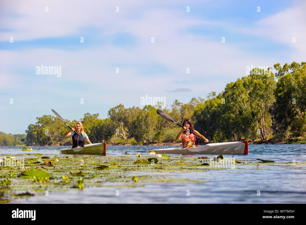 Two sporting sisters paddle down a freshwater river on a beautiful day. Stock Photo