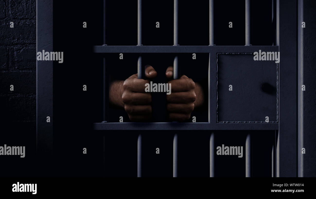 A closeup of a dimly lit prison holding cell door with a pair of african black hands holding onto the bars Stock Photo