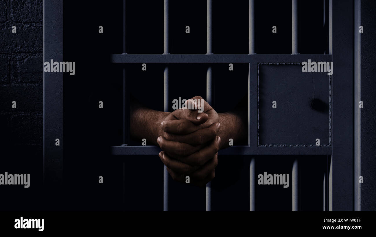 A closeup of a dimly lit prison holding cell door with a pair of african black hands reaching out in a clenched prayer position Stock Photo