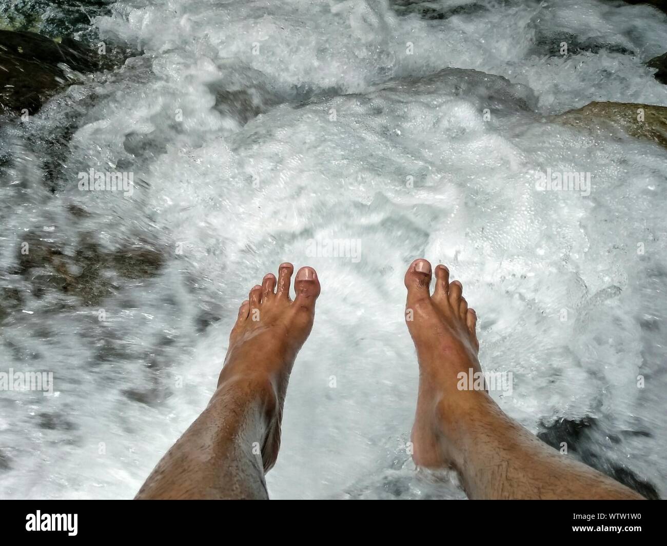 Low Section Of Feet Above Flowing Water Stock Photo