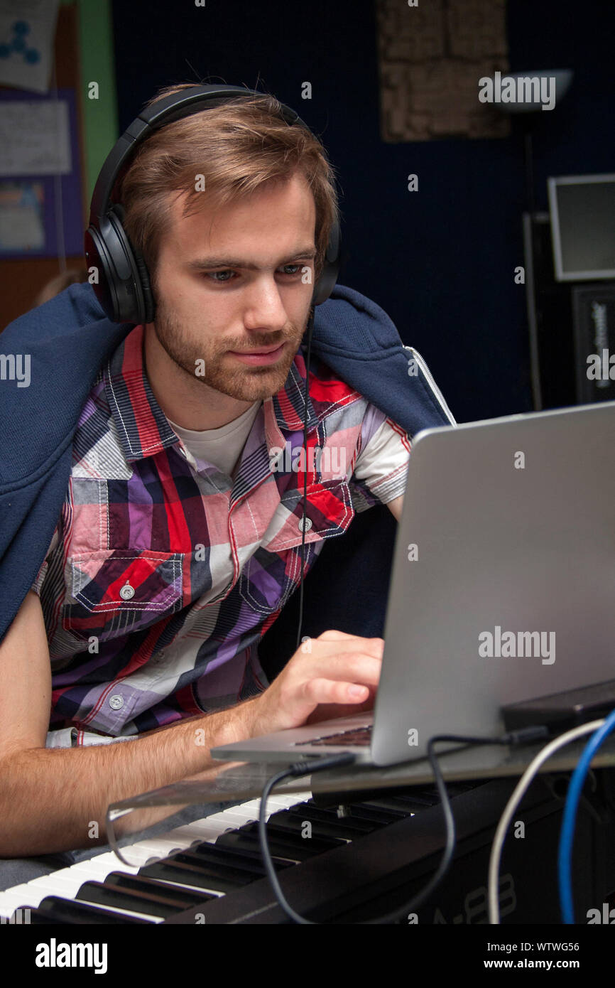 Focused young man in headphones composing on a laptop, piano, keyboard Stock Photo