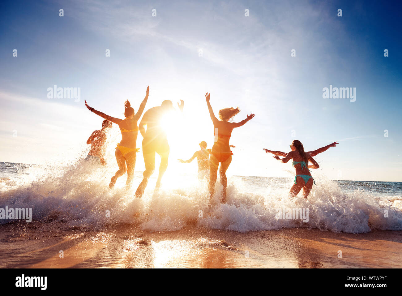 Big group of seven happy friends is having fun and runs at sunset beach to sun light and waves Stock Photo