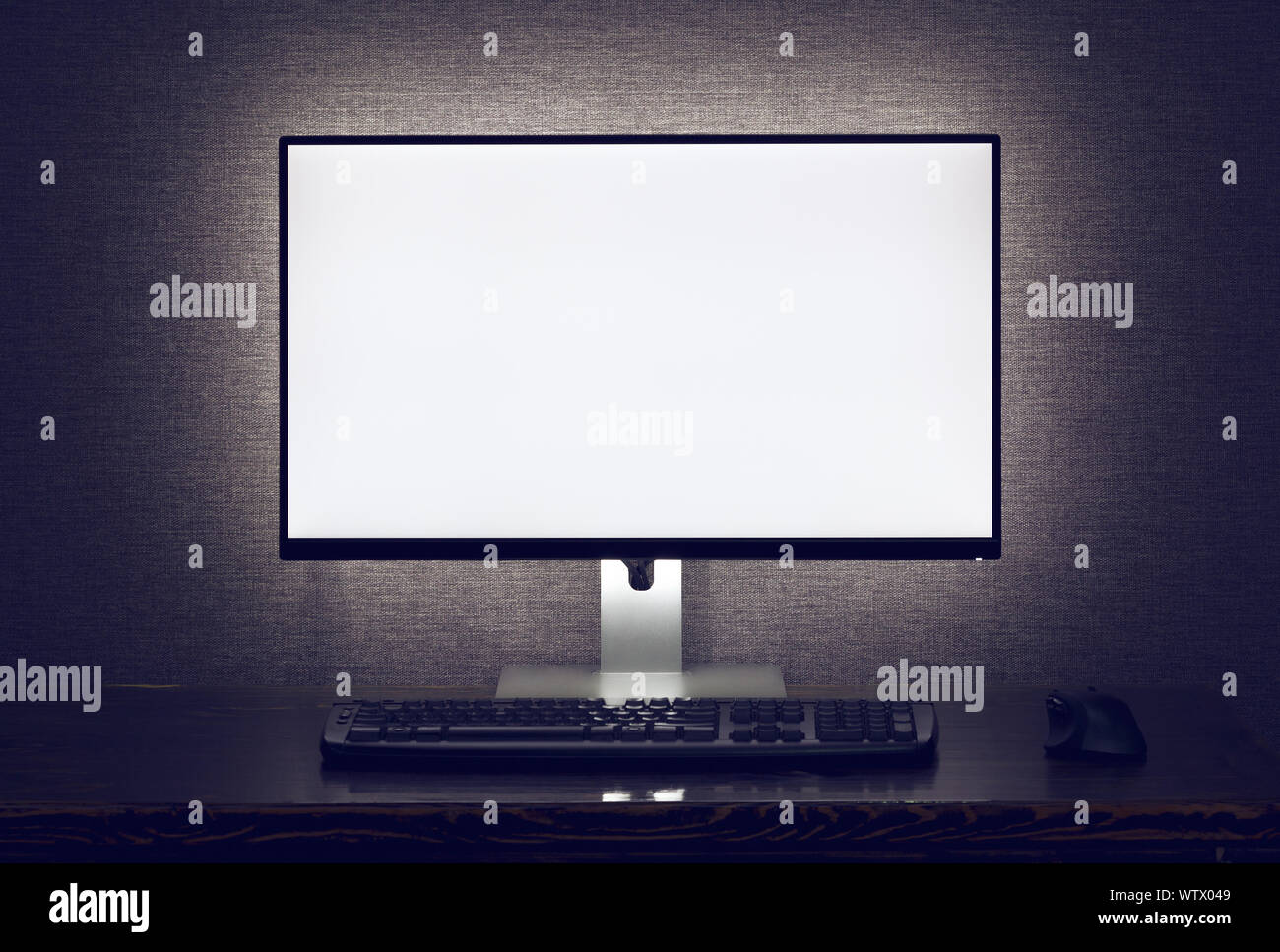 Blank monitor with keyboard and mouse with backlight over gray wall in dark room Stock Photo