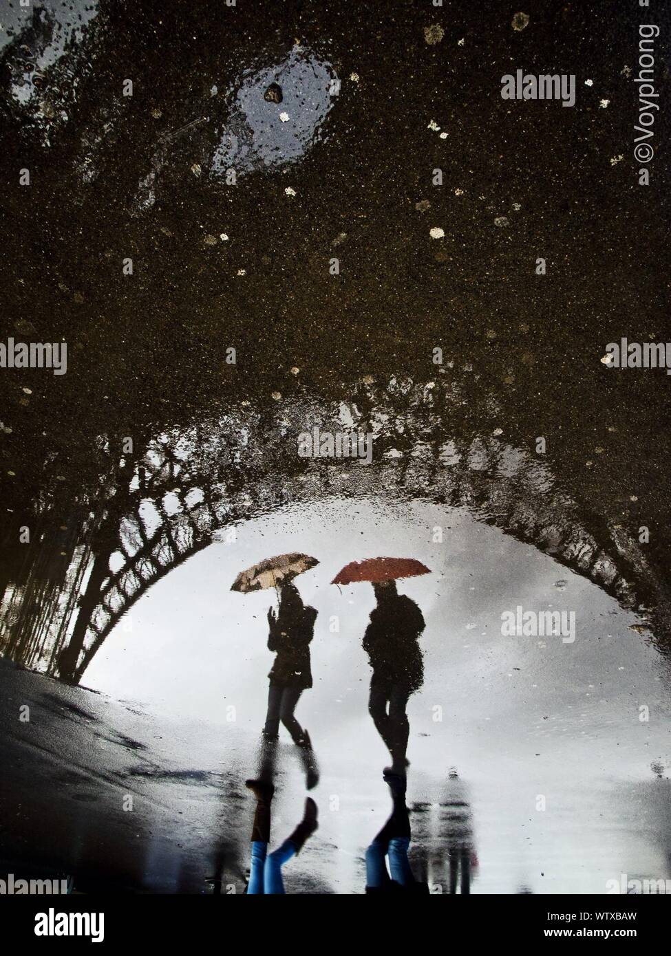 Reflection Of Eiffel Tower And Two People In Puddle Water Stock Photo