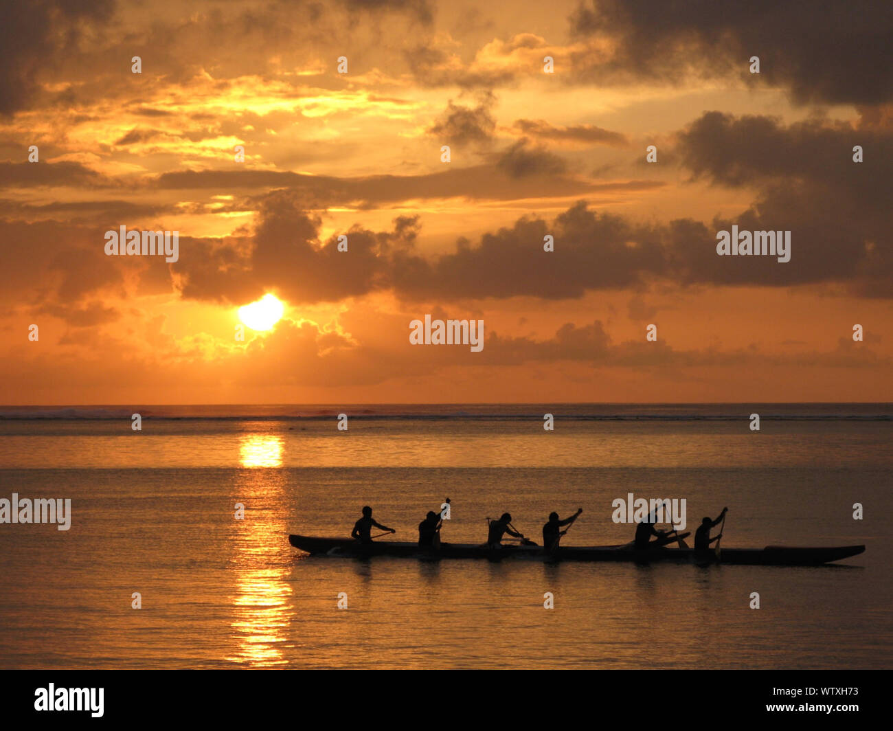 Silhouettes Of Six People On Canoe At Sunset Stock Photo