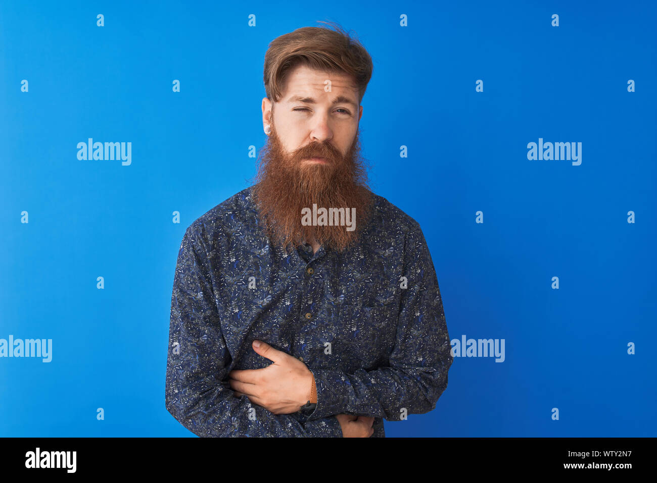 Young redhead irish man wearing floral summer shirt standing over isolated blue background with hand on stomach because nausea, painful disease feelin Stock Photo