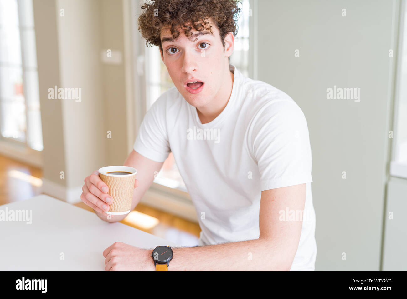 Young man drinking take away cup of coffee at home scared in shock with