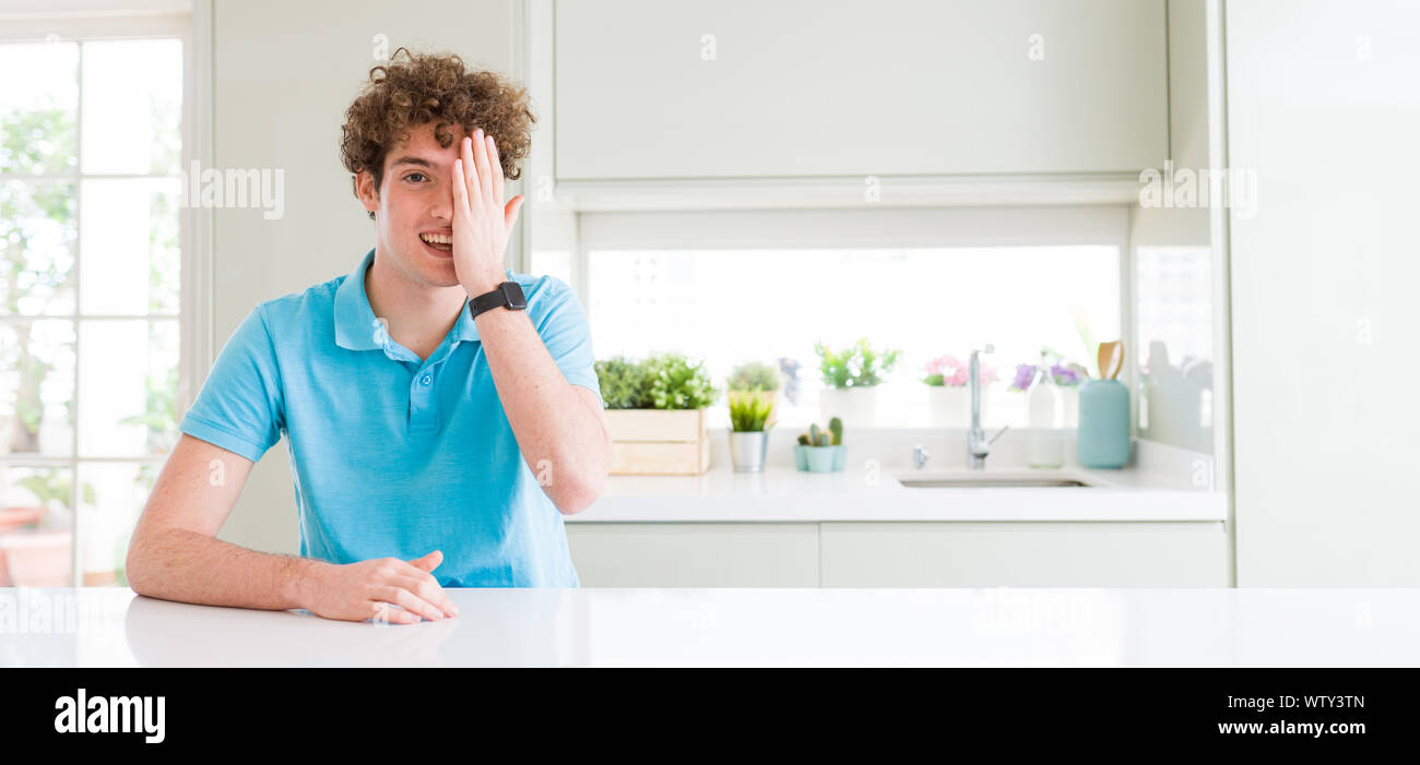 Wide shot of young handsome man at home covering one eye with hand with ...