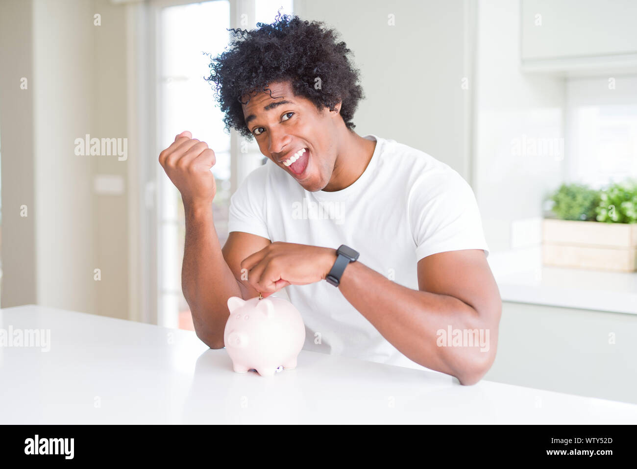 African American man putting a coin inside piggy bank screaming proud ...