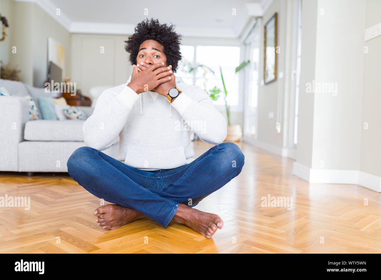 African American man sitting on the floor at home shocked covering ...