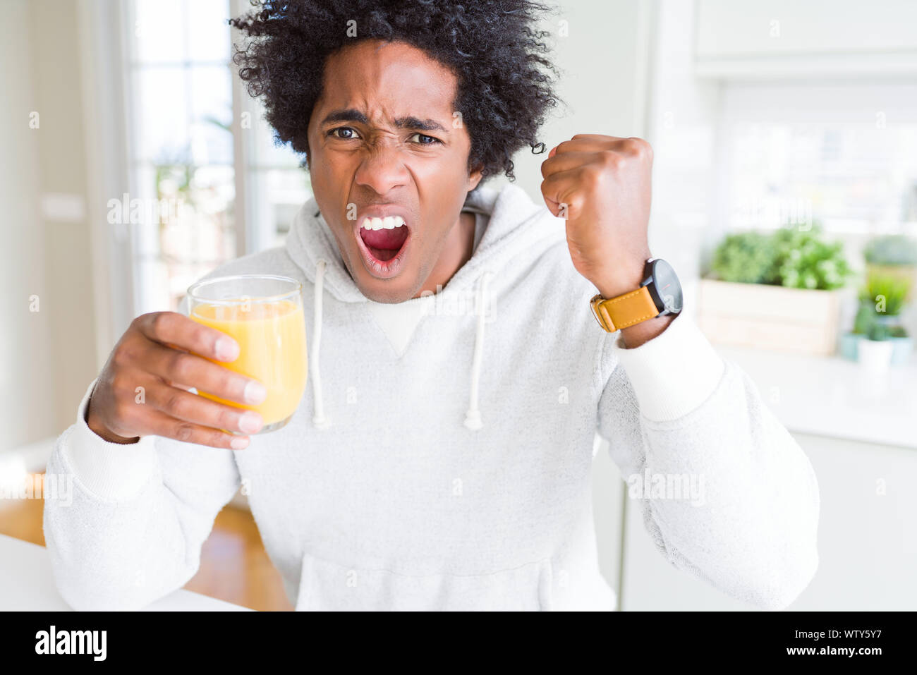 African American man holding and drinking glass of orange juice annoyed ...