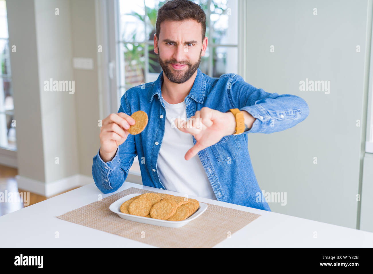 Handsome man eating healthy whole grain biscuit with angry face ...
