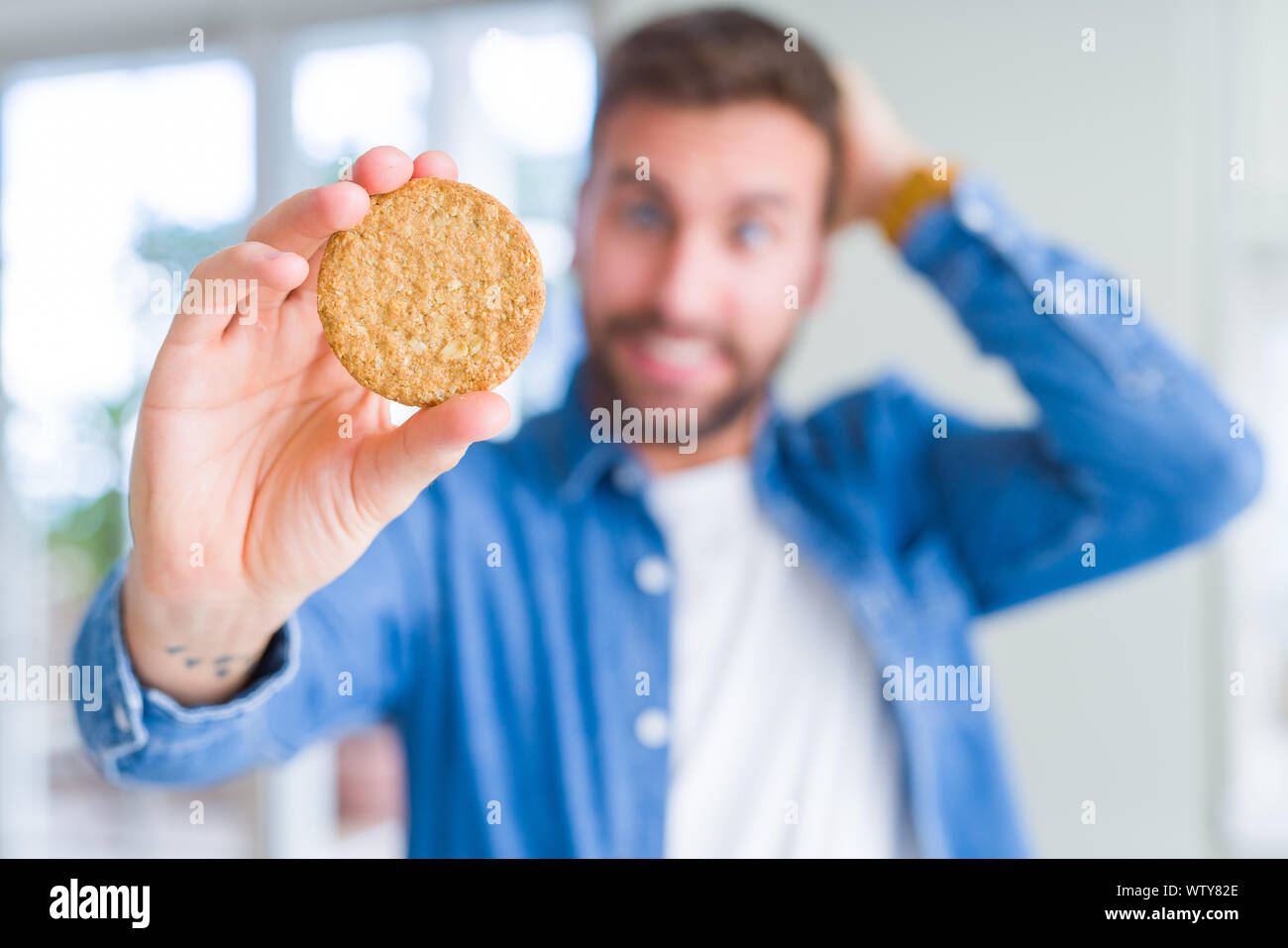 Handsome man eating healthy whole grain biscuit stressed with hand on