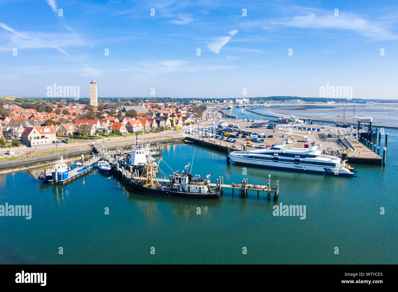 Netherlands, Terschelling - Aug 25, 2019: Brandaris lighthouse towers up. Catamaran MS Tiger moored to a wharf and other vessels along piers, in the h Stock Photo