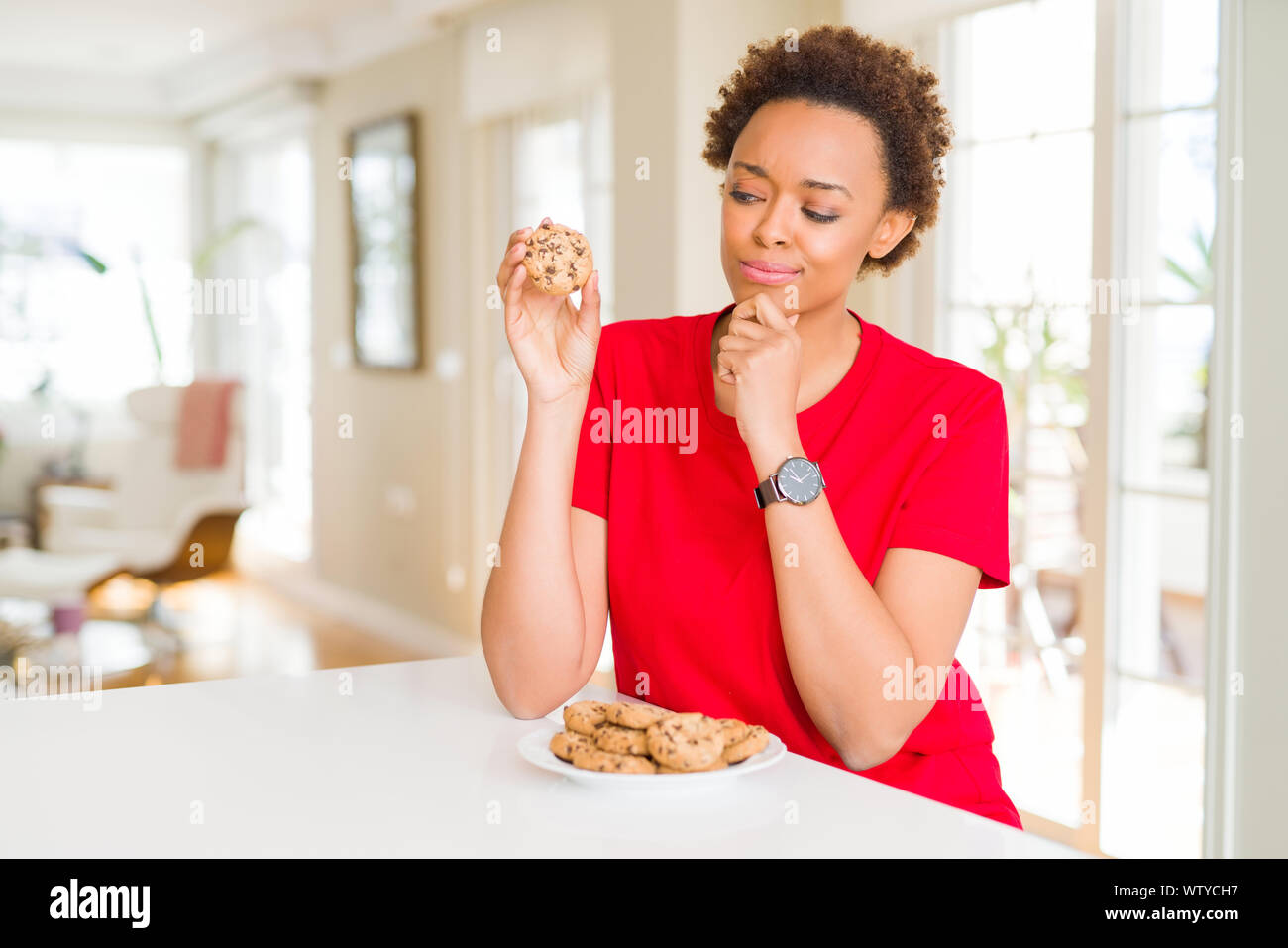 Young african american woman eating chocolate chips cookies serious