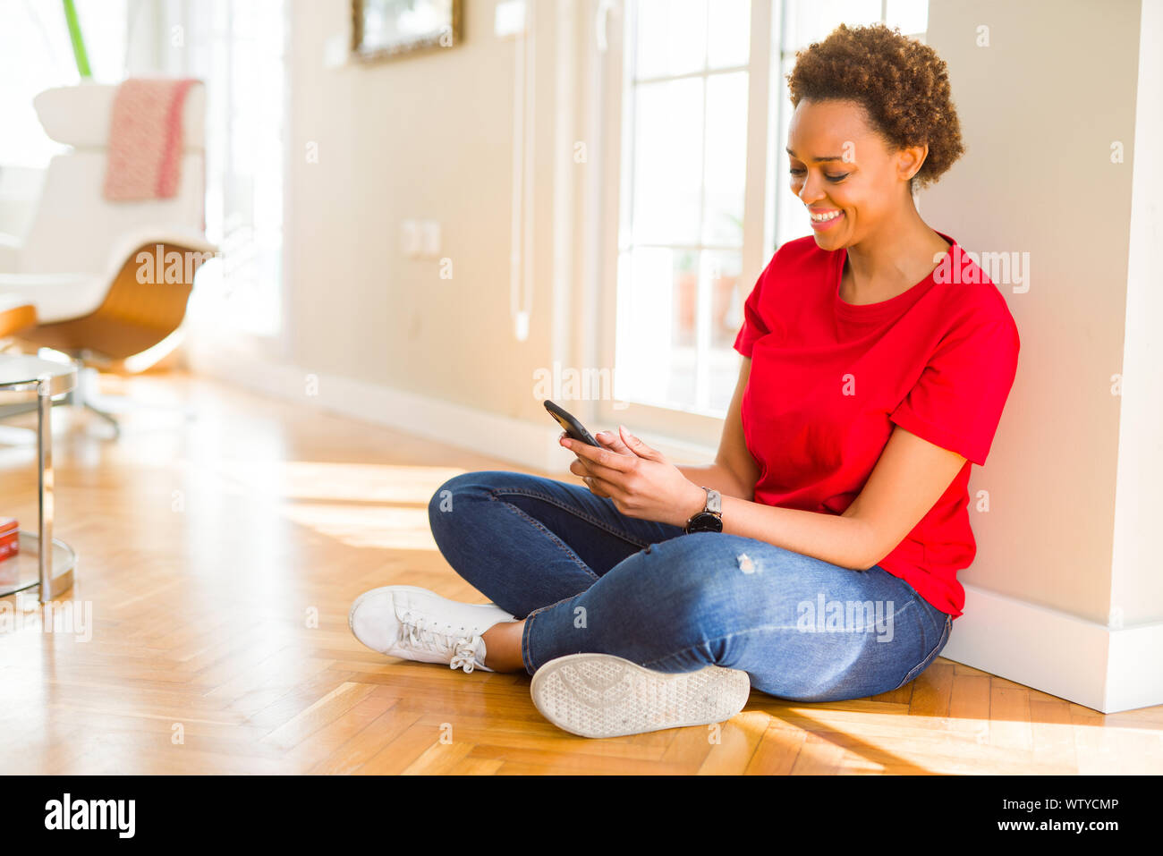 Beautiful young african american woman sitting on the floor using ...