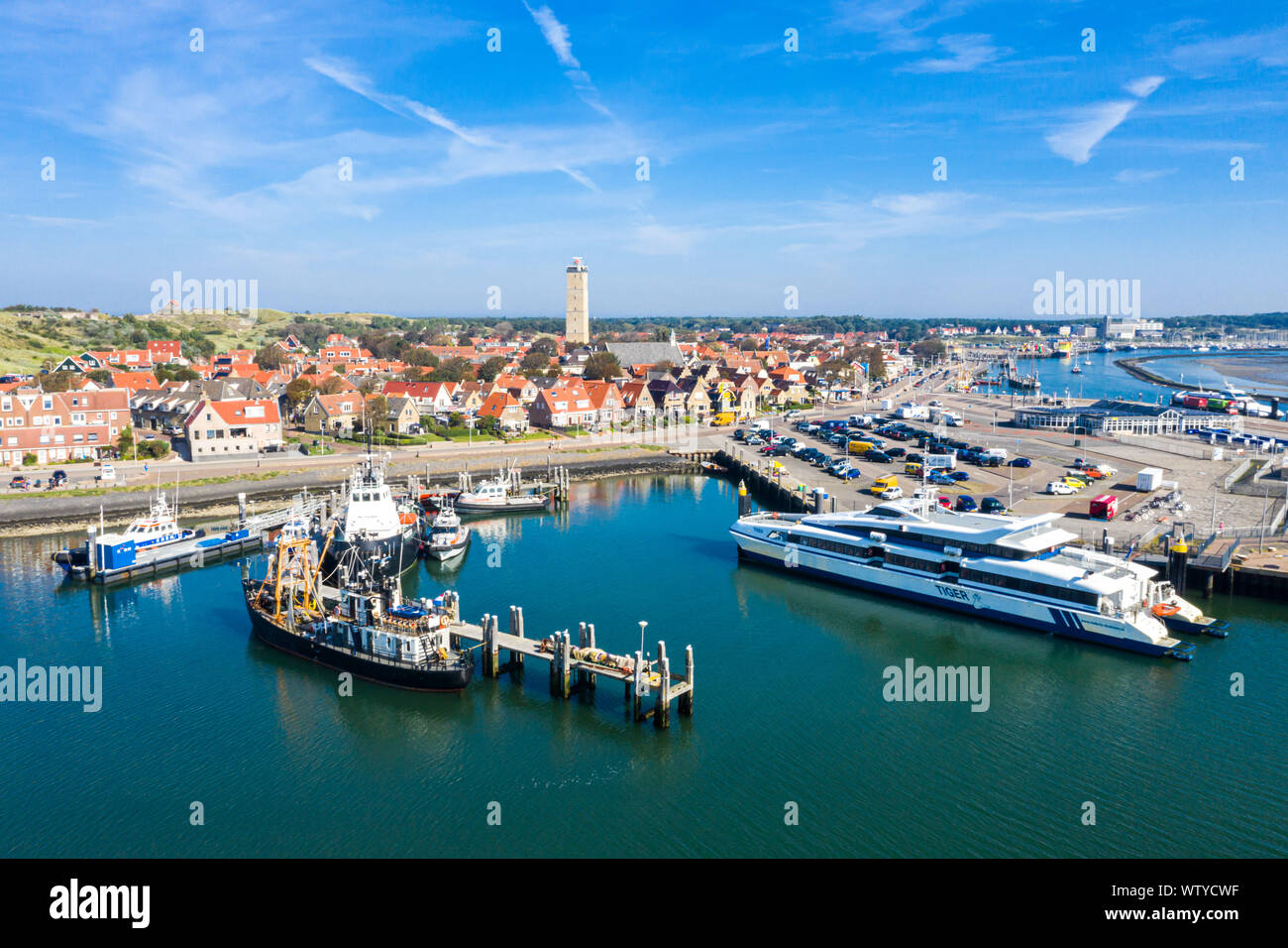 Netherlands, Terschelling - Aug 25, 2019: Brandaris lighthouse towers up. Catamaran MS Tiger moored to a wharf and other vessels along piers, in the h Stock Photo