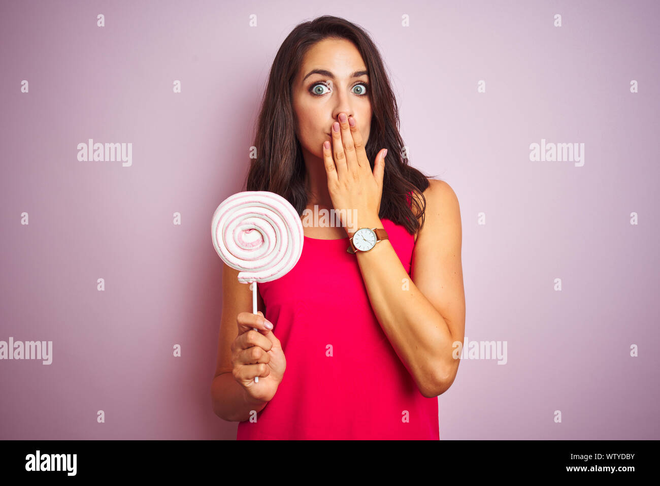 Young beautiful woman eating sweet candy over pink isolated background ...
