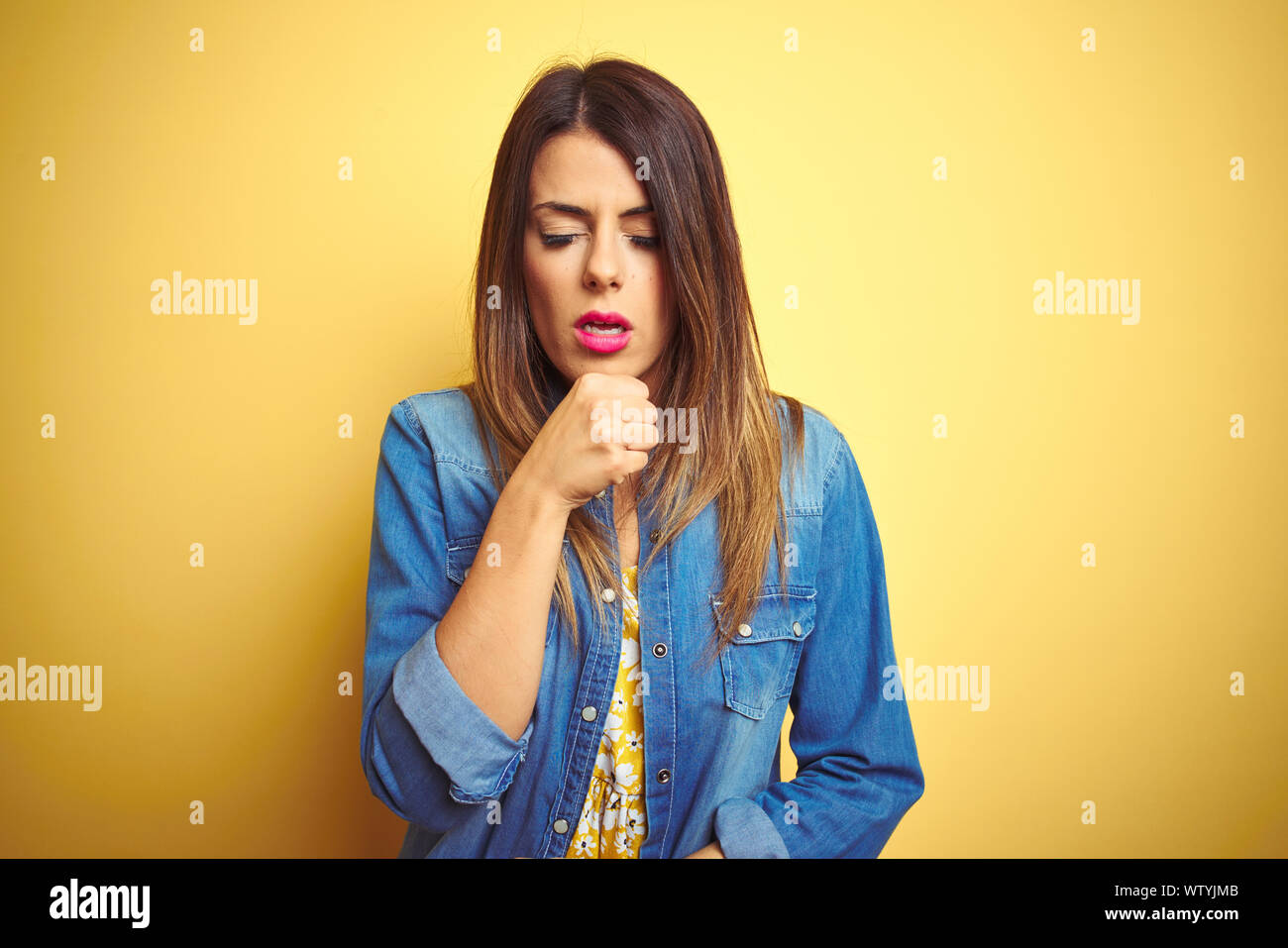 Young beautiful woman standing over yellow isolated background feeling unwell and coughing as symptom for cold or bronchitis. Healthcare concept. Stock Photo