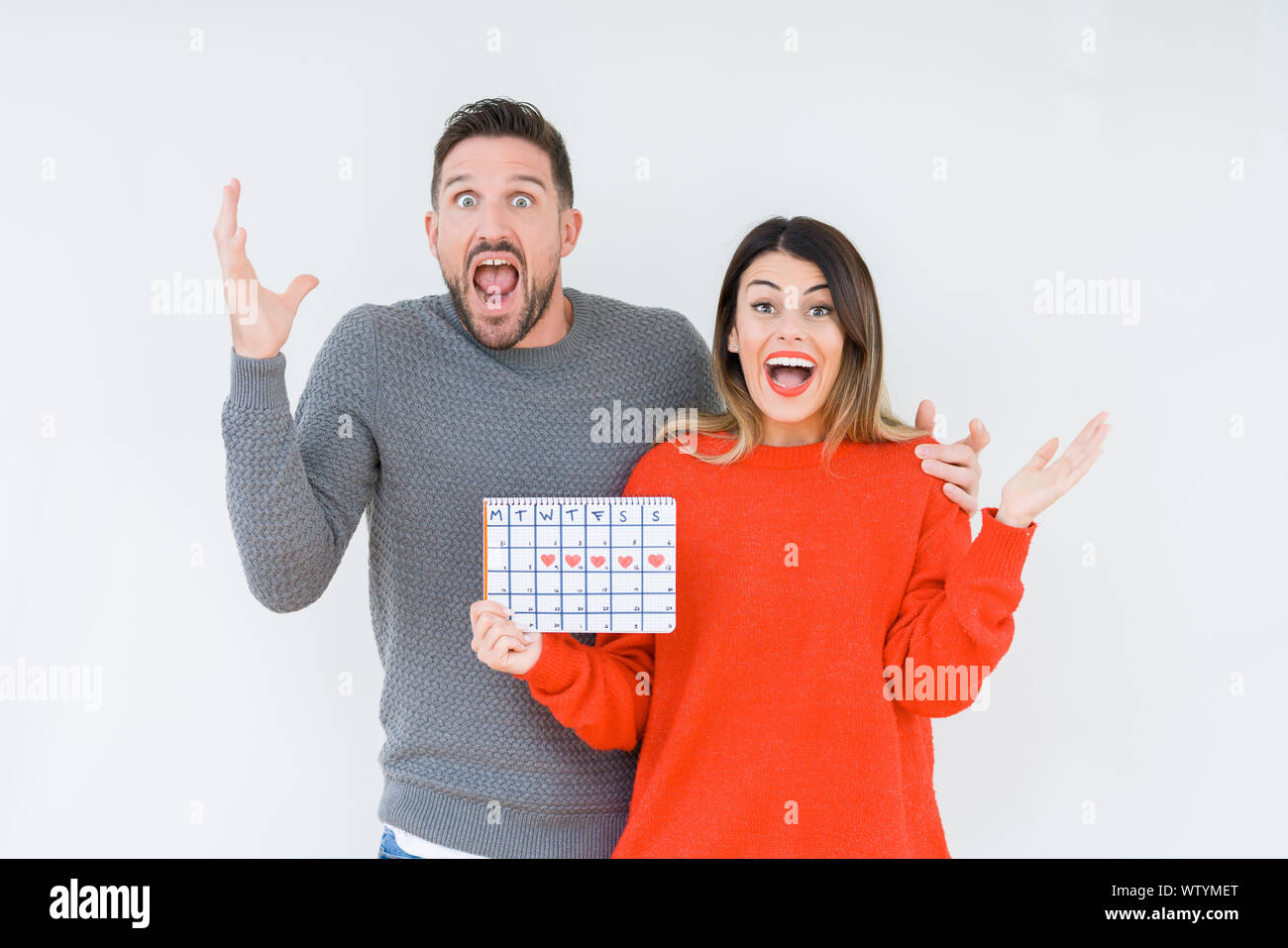 Young couple holding ovulation calendar over isolated background very happy and excited, winner ...