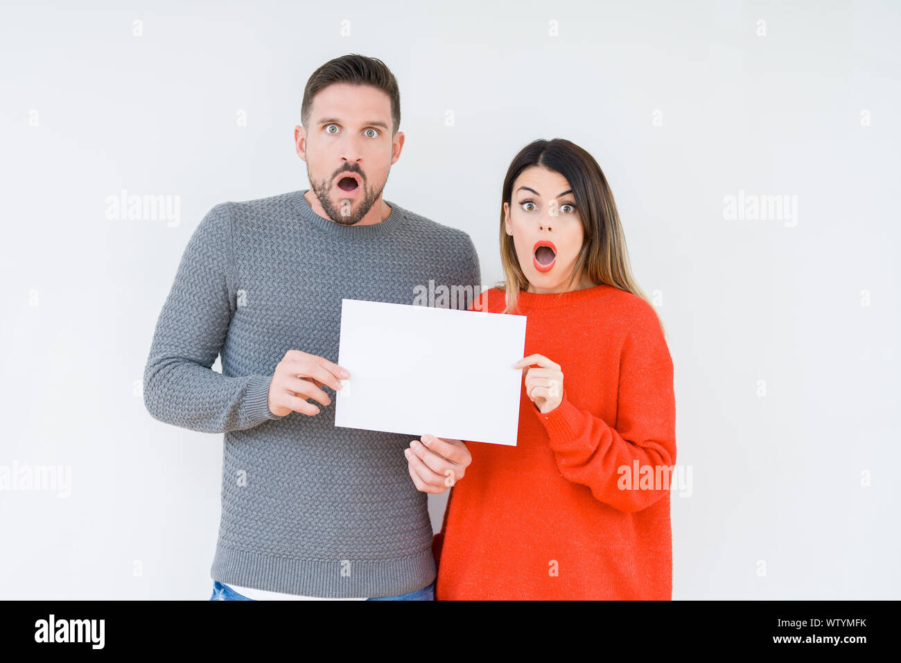 Afraid Paper Young couple holding blank sheet paper over isolated background scared ...