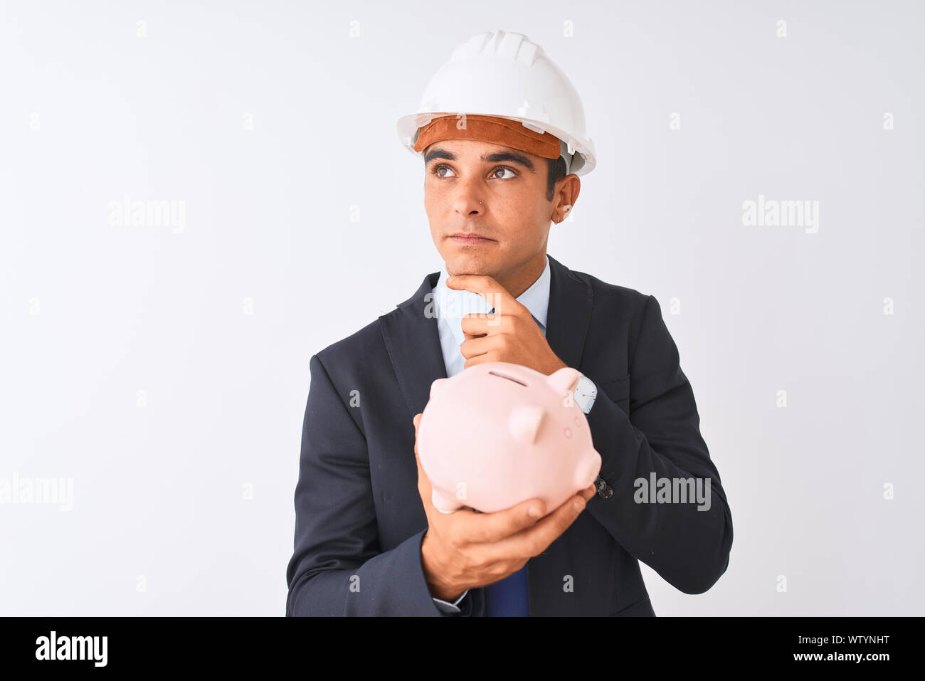 Handsome architect man wearing helmet holding piggy bank over isolated ...