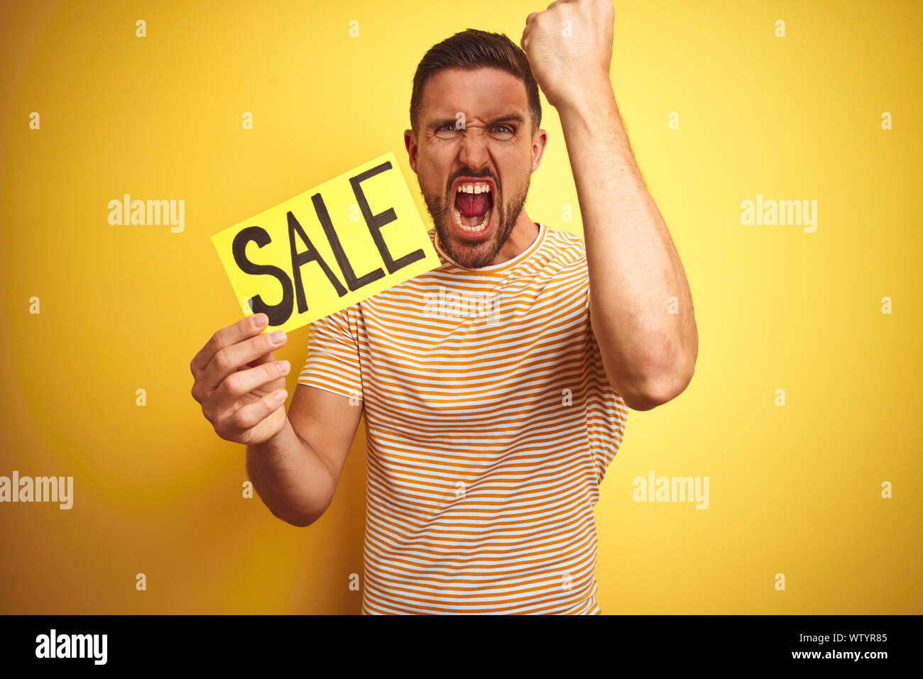 Young man holding sale advertising poster board over yellow isolated