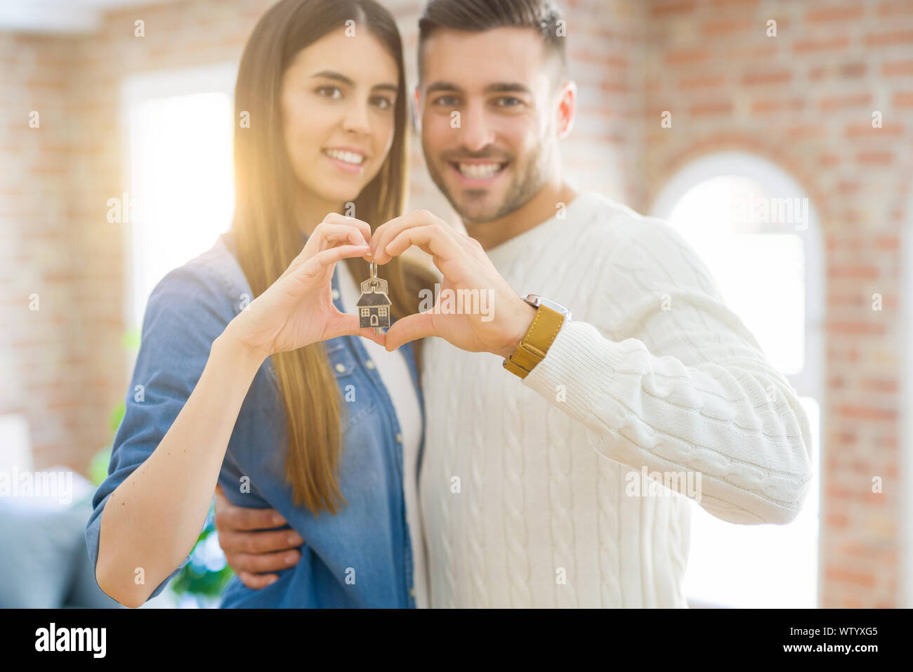 Young couple moving to a new home, hugging in love showing keys of new ...