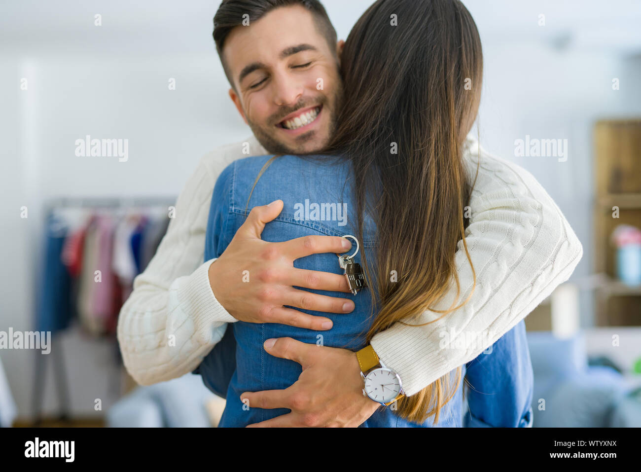 Young couple moving to a new home, hugging in love showing keys of new ...