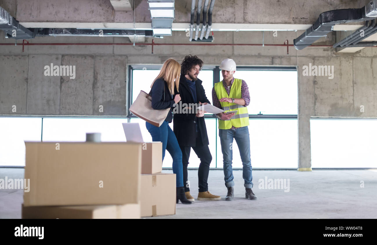 architect using tablet computer while showing house design plans to a young couple at construction site Stock Photo