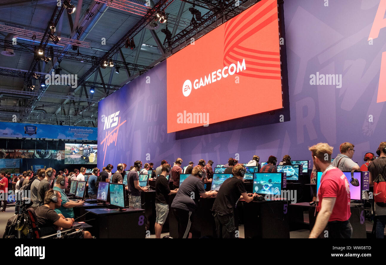 visitors play car racing game  below large screen displaying the word „gamescom“ at gamescom , world’s largest trade fair for computer and video games in Cologne, Germany on  August 21, 2019 Stock Photo