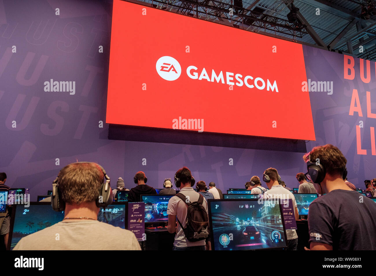 visitors play car racing game  below large screen displaying the word „gamescom“ at gamescom , world’s largest trade fair for computer and video games in Cologne, Germany on  August 21, 2019 Stock Photo