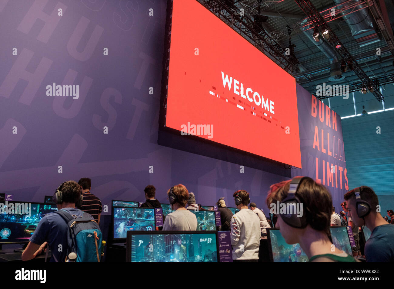 visitors play car racing game  below large screen displaying the word „Welcome“ at gamescom , world’s largest trade fair for computer and video games in Cologne, Germany on  August 21, 2019 Stock Photo