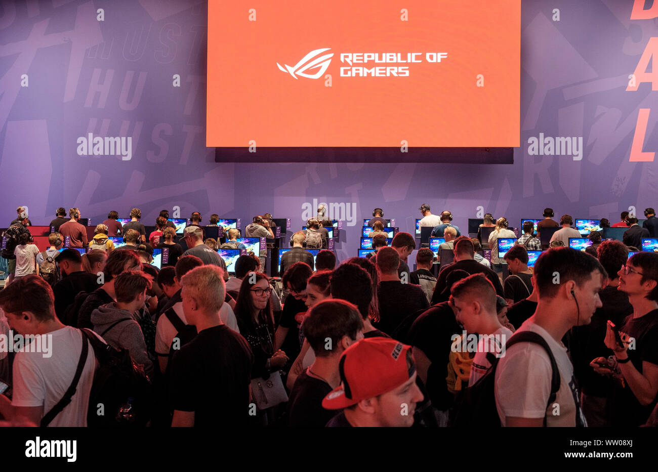 visitors play car racing game  below large screen displaying the phrase „Republic of Gamers“ at gamescom , world’s largest trade fair for computer and video games in Cologne, Germany on  August 21, 2019 Stock Photo
