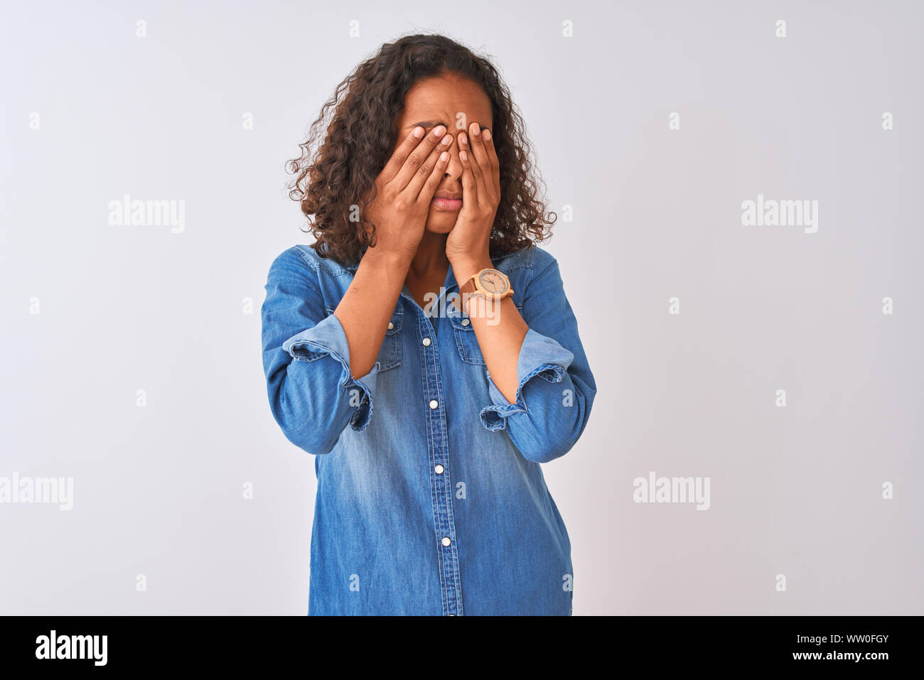 Young brazilian woman wearing denim shirt standing over isolated white background rubbing eyes for fatigue and headache, sleepy and tired expression. Stock Photo