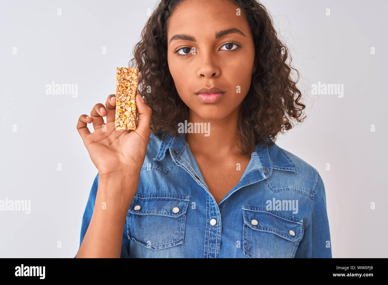 Young brazilian woman eating granola bar standing over isolated white