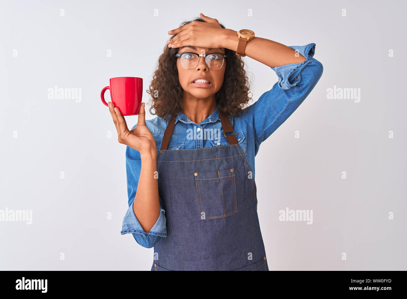 Brazilian barista woman wearing apron drinking cup of coffee over isolated white background stressed with hand on head, shocked with shame and surpris Stock Photo