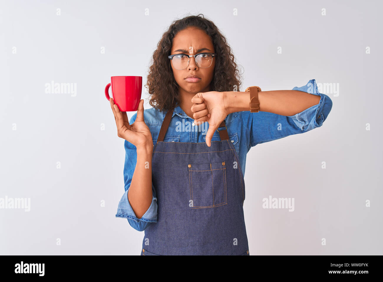 Brazilian barista woman wearing apron drinking cup of coffee over isolated white background with angry face, negative sign showing dislike with thumbs Stock Photo