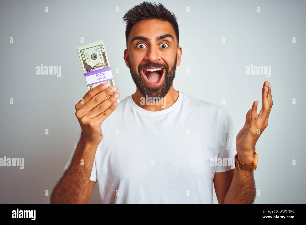 Young indian man holding dollars standing over isolated white ...
