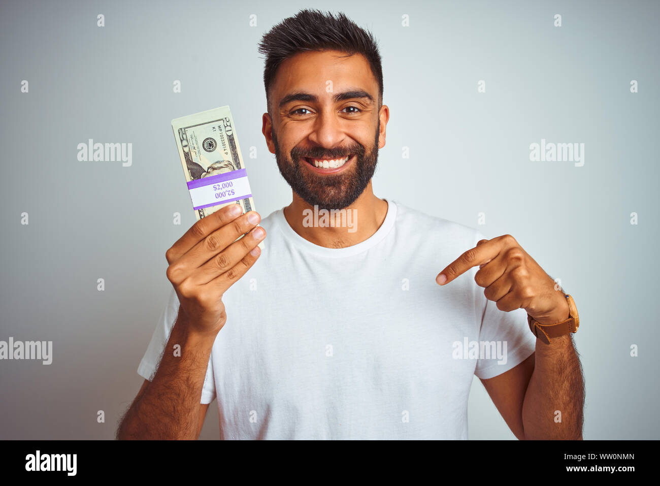 Young indian man holding dollars standing over isolated white ...