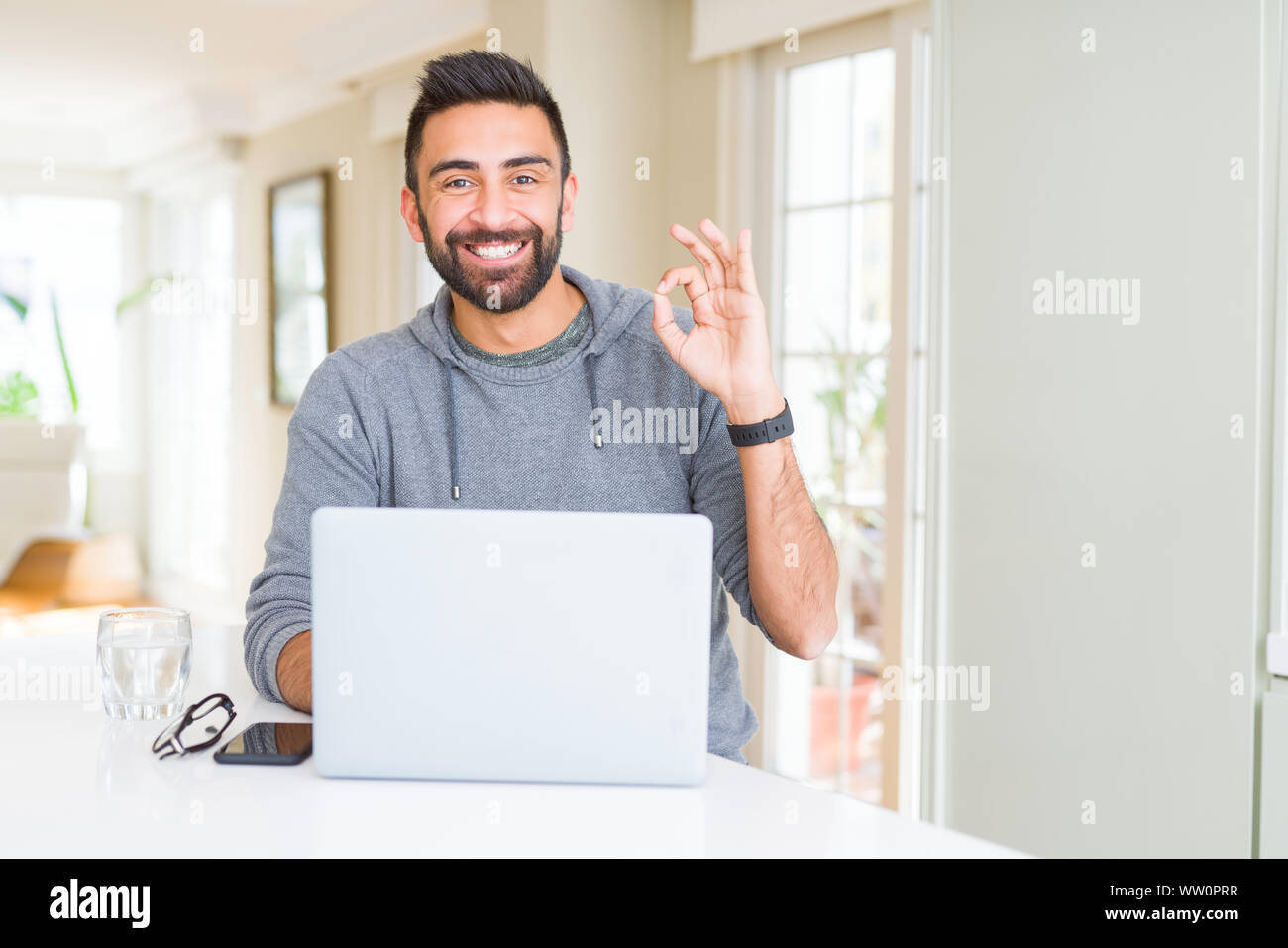 Hispanic Man Using Computer Handsome hispanic man working using computer laptop doing ok sign with ...