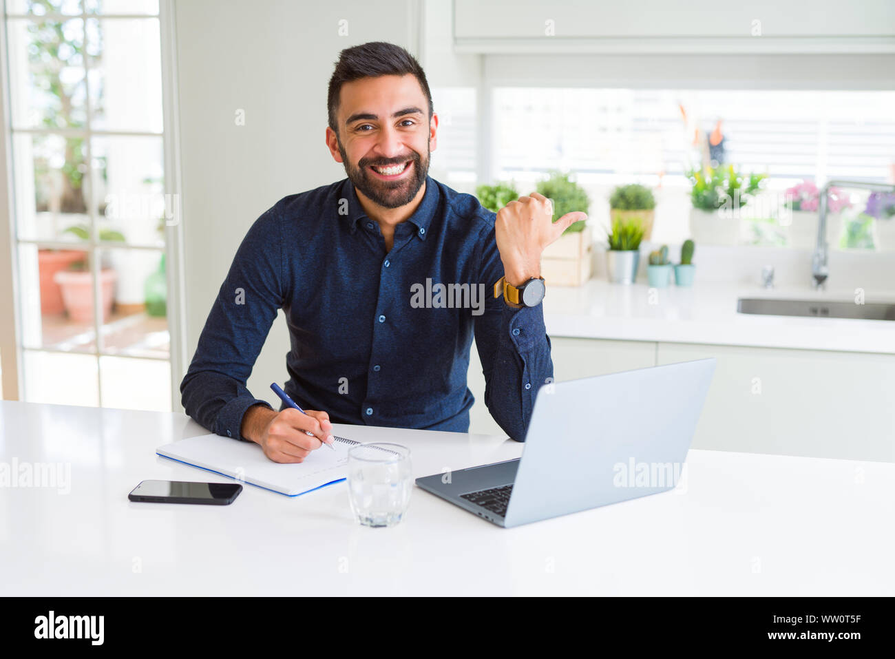 Handsome hispanic man working using computer and writing on a paper ...