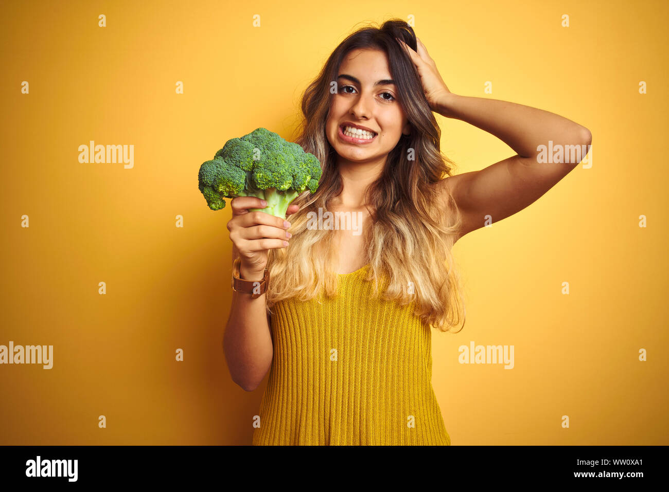 Young beautiful woman eating broccoli over yellow isolated background