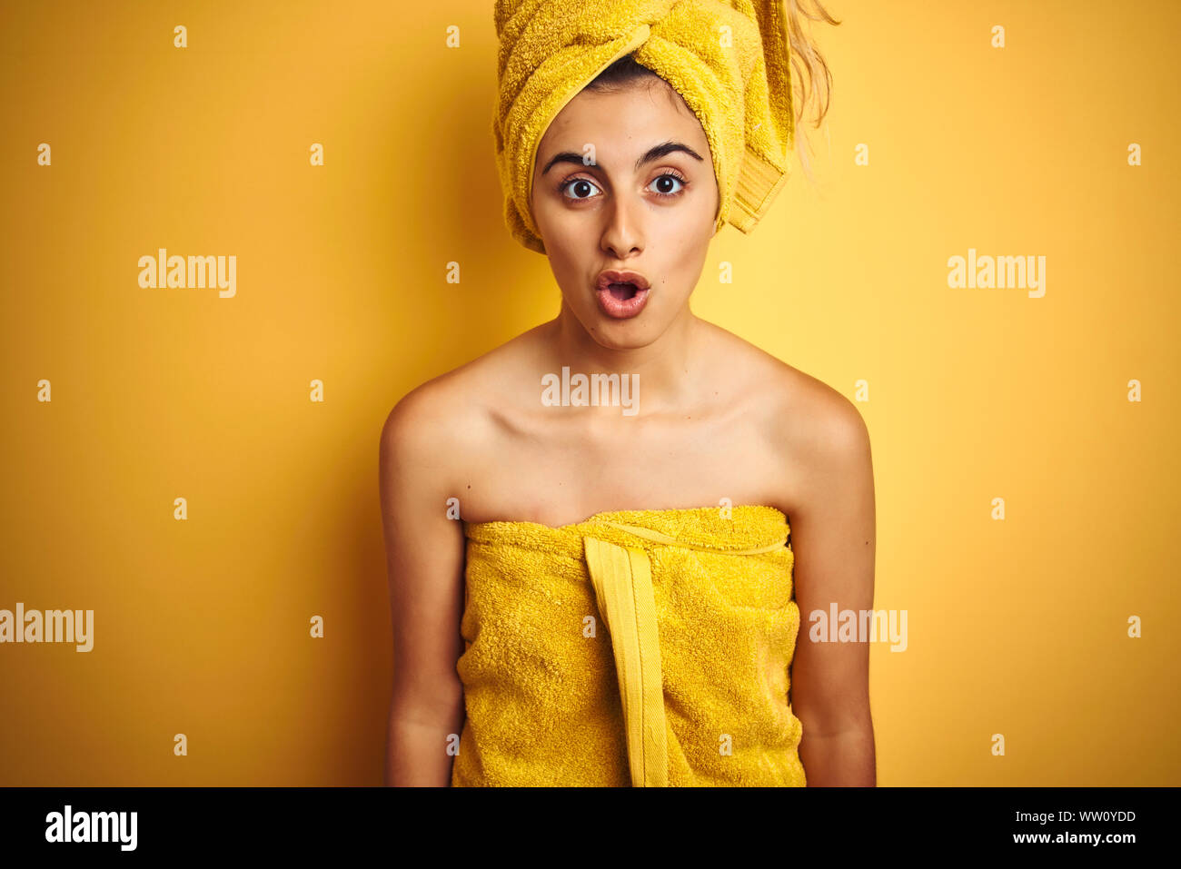 Young beautiful woman wearing a shower towel after bath over yellow