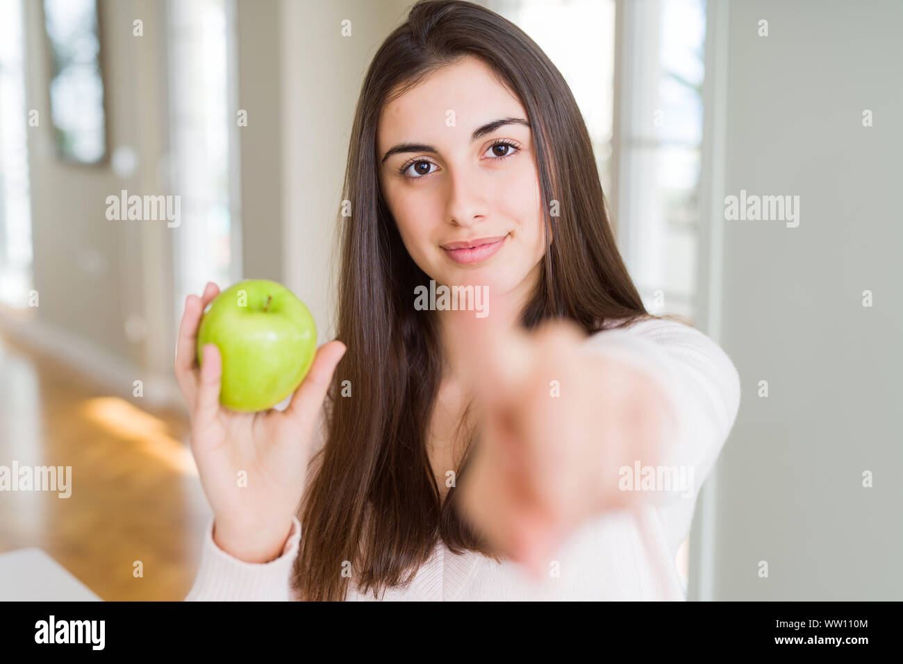 Beautiful young woman eating healthy green apple fruit pointing with ...