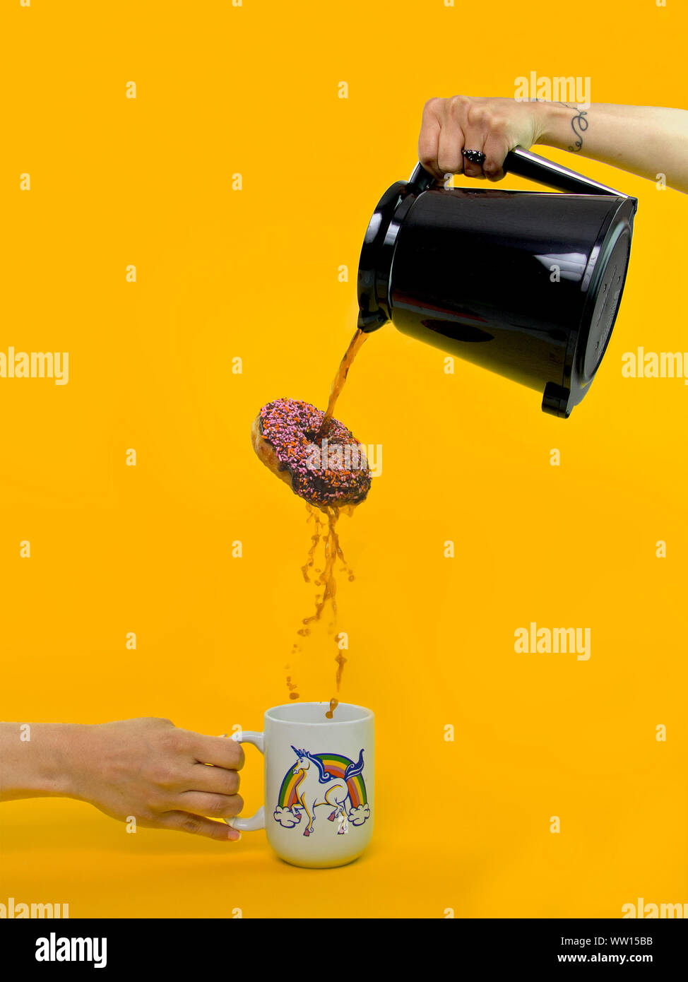 Cropped Image Of Hand Pouring Coffee Through Donut Hole Against Yellow Background Stock Photo