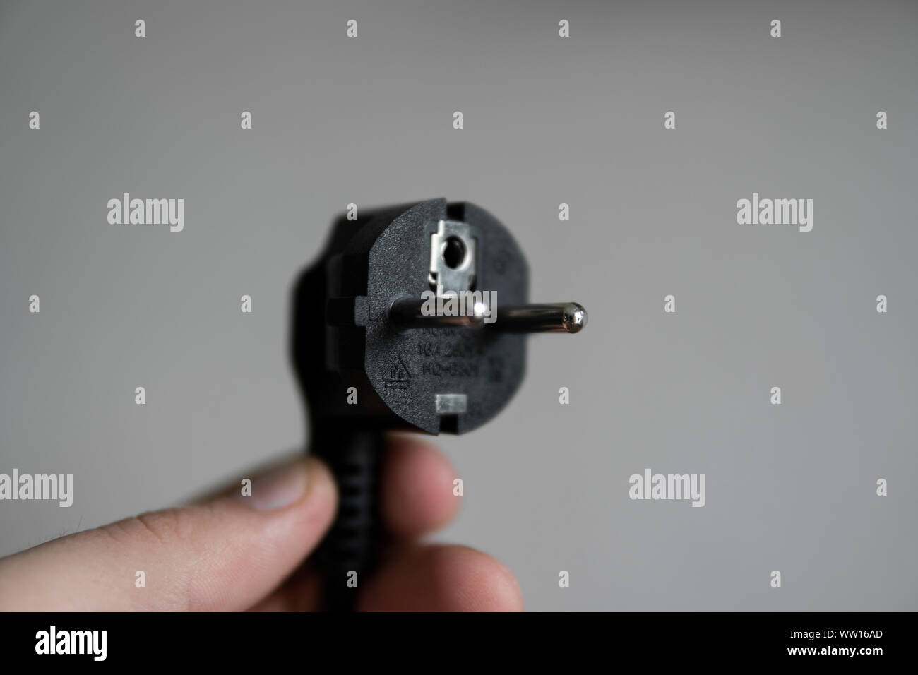 Hand holding black electric plug on a grey background. Stock Photo